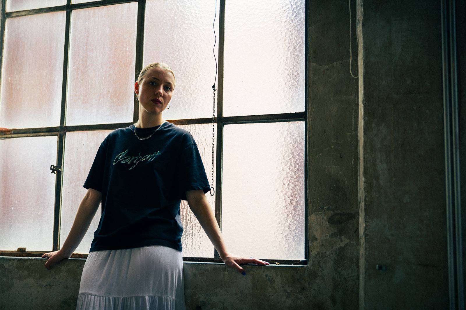 Frau im Carhartt-Shirt vor Industriefenster, Gegenlicht