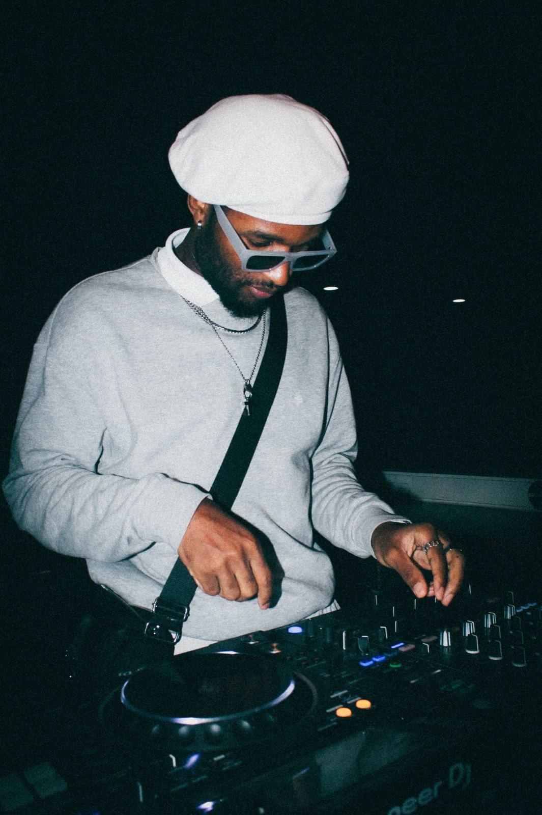 DJ mit weißer Mütze und Sonnenbrille am Pioneer-Controller, dunkler Hintergrund
