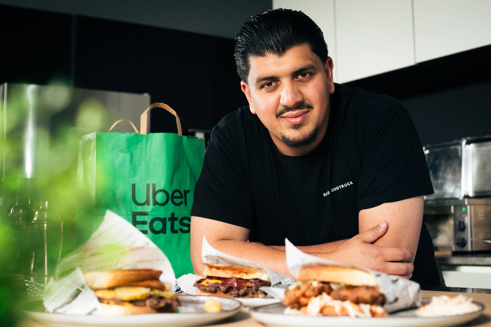 Mann hinter Burgern und Uber-Eats-Tüte, lächelnd in die Kamera