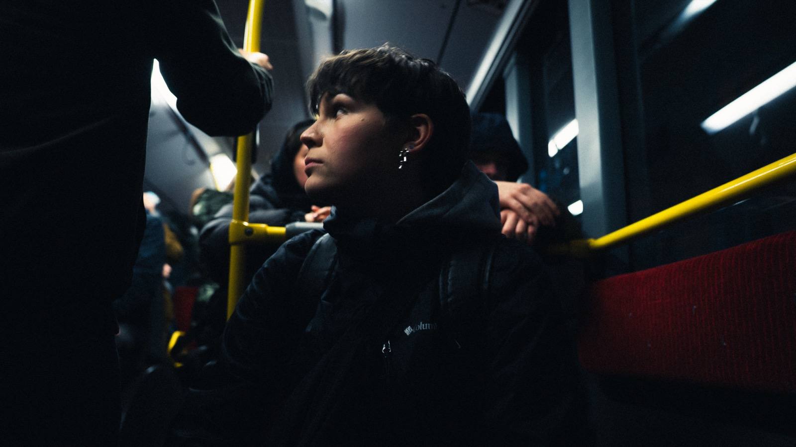 Junge Frau in der Nacht im Bus, gelbe Haltestangen, cinematische Atmosphäre