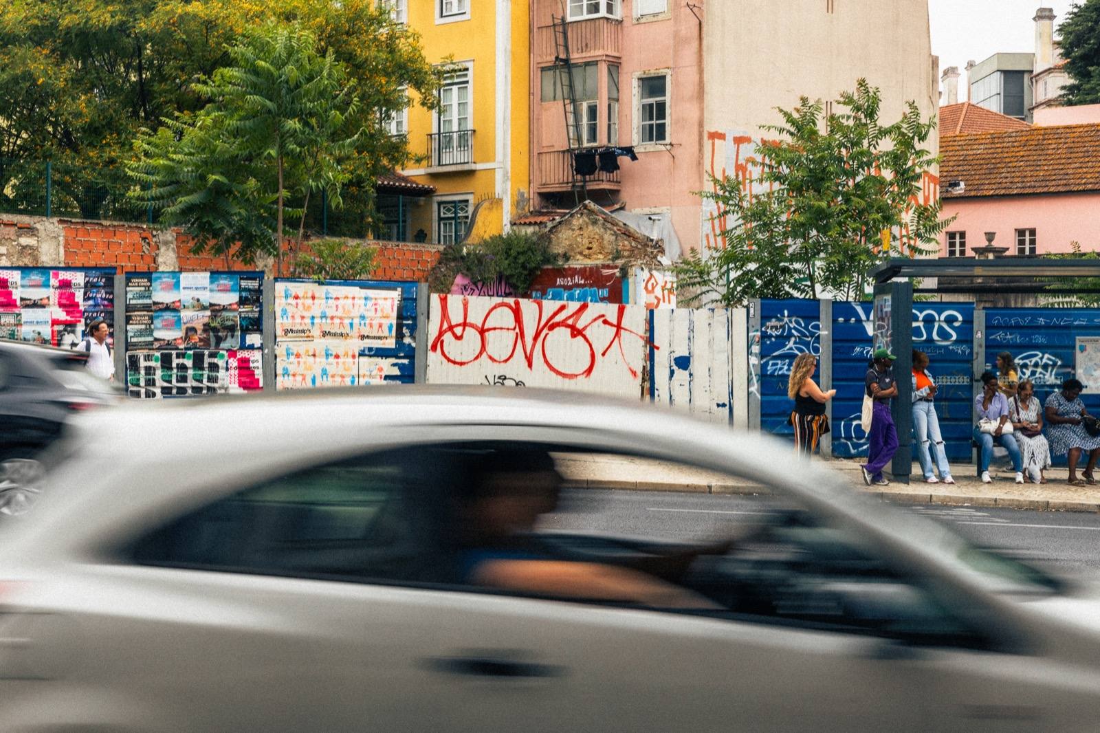 Vorbeifahrendes Auto mit Bewegungsunschärfe, Bushaltestelle und bunte Häuser in Lissabon